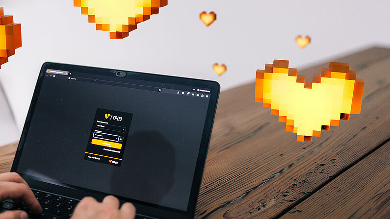 Zwei Hände tippen auf einem Laptop, der das TYPO3-Login-Fenster zeigt. Im Raum um den Bildschirm schweben gelbe Herzen im Pixel-Art-Stil über einem Holztisch. 
