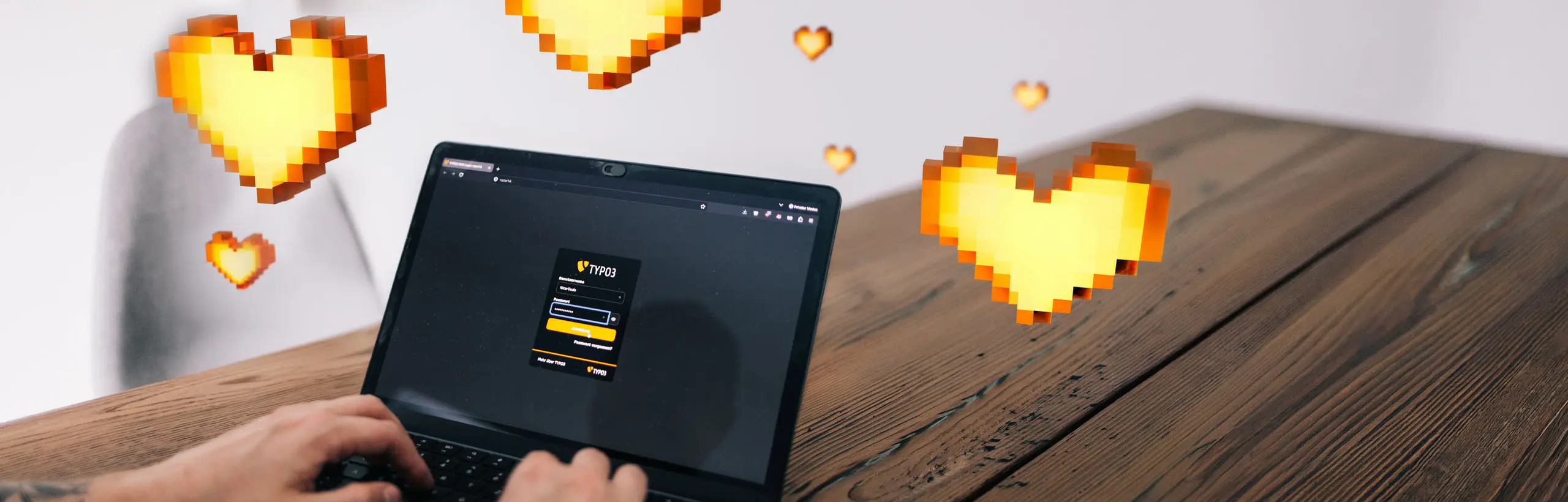 Zwei Hände tippen auf einem Laptop, der das TYPO3-Login-Fenster zeigt. Im Raum um den Bildschirm schweben gelbe Herzen im Pixel-Art-Stil über einem Holztisch. 