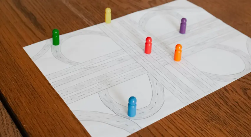 Die Nahaufnahme aus schräger Vogelperspektive zeigt ein DIN-A4-Blatt mit der Zeichnung eines Autobahnkreuzes. An mehreren Stellen der Fahrbahnen stehen Spielfiguren.