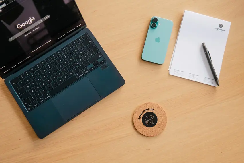 Vogelperspektive eines Schreibtischs mit Laptop, Smartphone, Nozitblock und Untersetzer mit NFC-Technologie